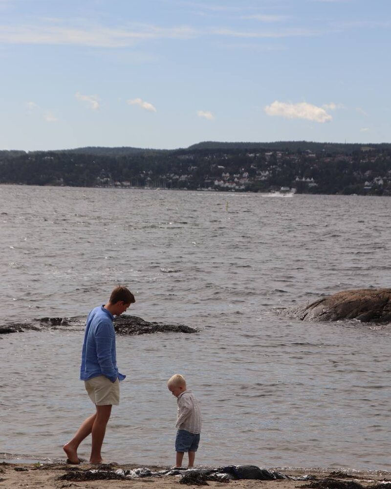En voksen og et barn som står ved vannkanten på stranden